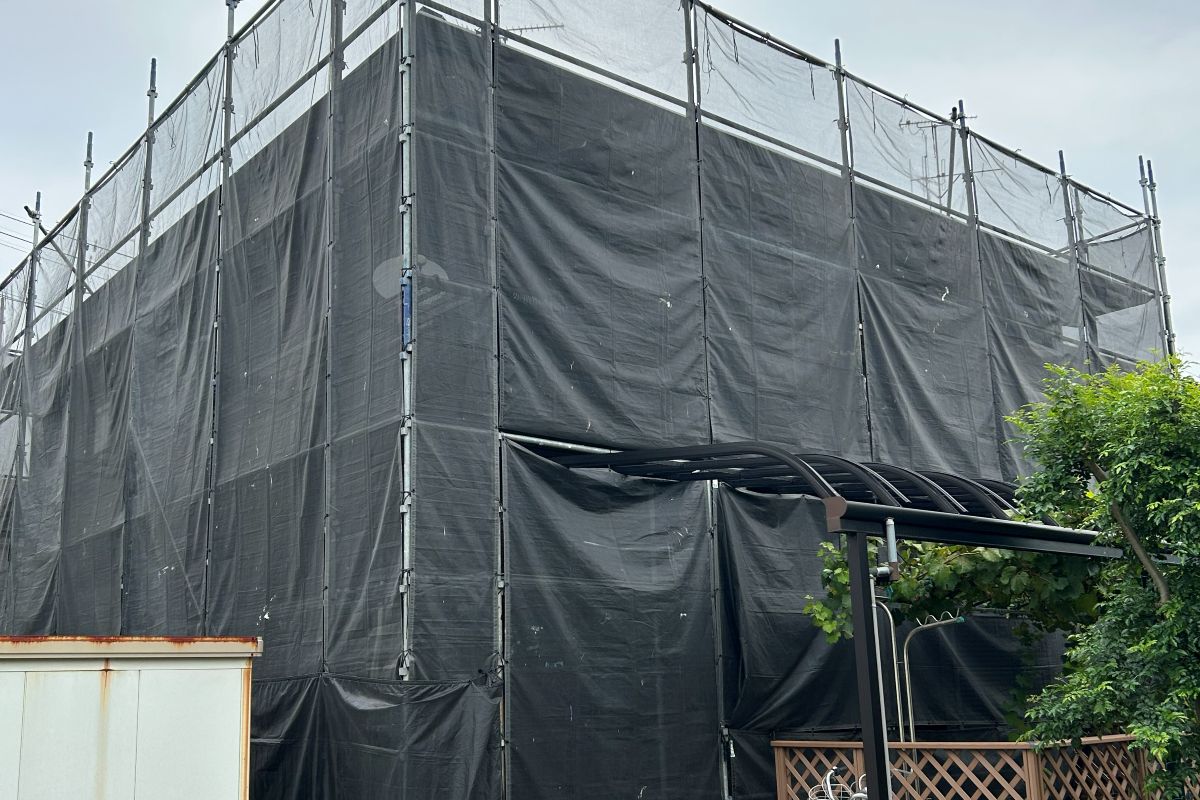 足場と黒いメッシュシートにすっぽり覆われた塗装工事中のわが家(筆者撮影)