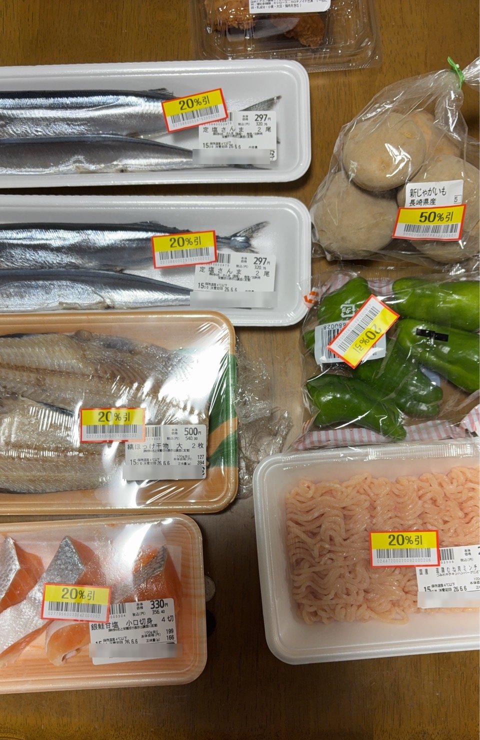 スーパーで買った値引き品。定塩さんま2尾297円やほっけの干物、銀鮭、鶏むねミンチ、新じゃがいも、ピーマンに20〜50%引きのシールが貼られている(筆者撮影)
